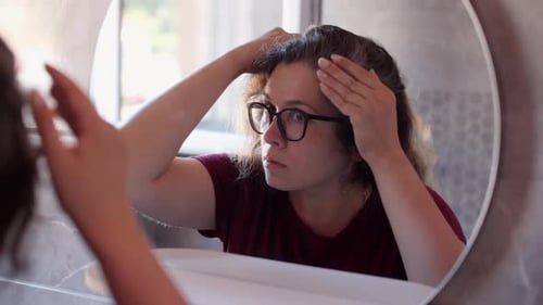 Woman Examines Gray Hair Roots in Mirror