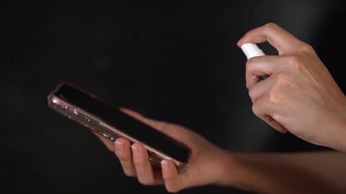Woman Sprays Disinfectant onto Smartphone Screen