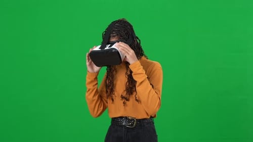 Absorbed African American Teenage Girl in VR Headset Pointing Around Turning on Green Screen