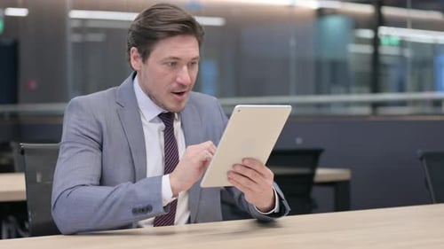 Excited Businessman Using Tablet in Modern Office