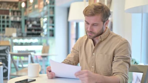 Professional Young Man Reading Documents in Cafe