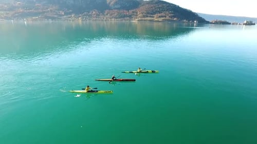 Three kayakers paddle in a scenic mountain lake.