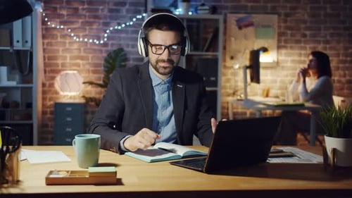 Guy in Headphones Enjoying Music in Office Busy Working with Laptop at Night