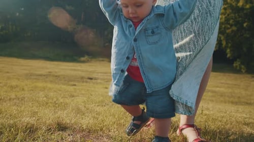Child Takes the First Steps Walking in the Park with Mom