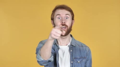Hombre pelirrojo apuntando a la cámara sobre fondo amarillo