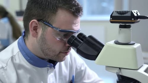 Portrait of Male Scientist Looking Through Microscope Sitting at Table in Pharmaceutical Lab Spbas