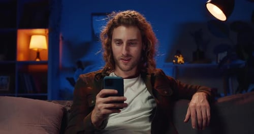 Man Relaxing on Couch Using Smartphone at Night
