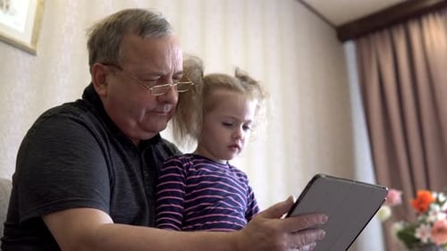 Grandfather and Granddaughter Use Tablet Together Indoors