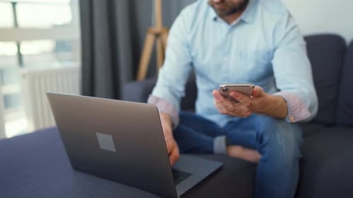 Man Using Smartphone and Laptop at Home
