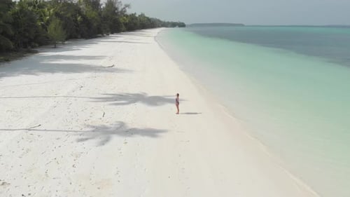 Aerial: Woman relaxing on white sand beach turquoise water tropical coastline