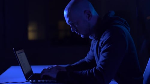 Man Typing on Laptop in Dark, Blue Lit Room