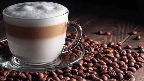 Tasse mit heißem Cappuccino-Getränk auf gerösteten Kaffeebohnen. dolly shot