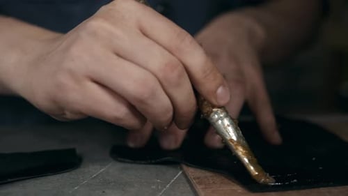 Hands Applying Glue to Leather Material