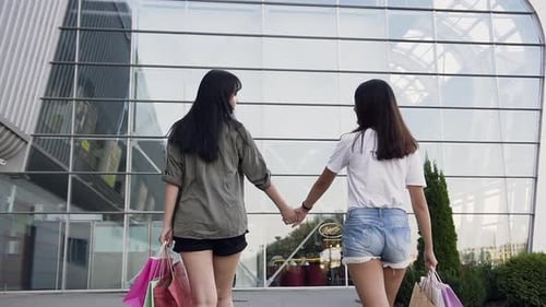 Beautiful Slender Asian Women Holding by Hands and Walking Near Modern Building