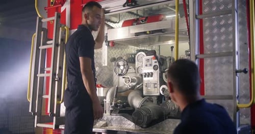 Fireman Teaching Trainee To Use Fire Engine Equipment