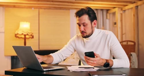 Adult Using Phone and Laptop at Table