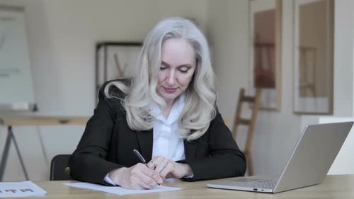 Elegant Woman Writing at Desk in Bright Office