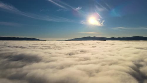 Luftaufnahme des lebendigen Sonnenuntergangs über weißen, dichten Wolken mit fernen dunklen Bergen am Horizont