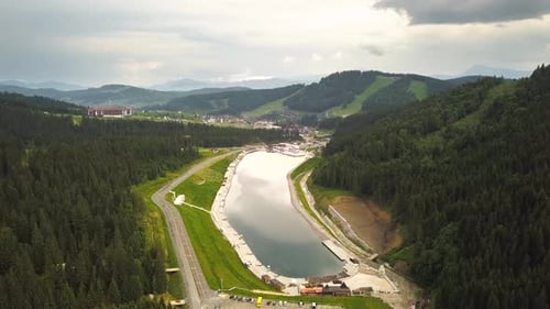 Aerial view of a big lake surrounded with high green mountains covered in spruce forest