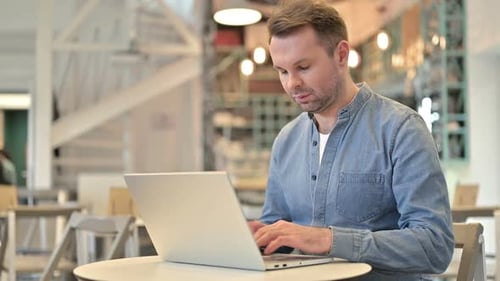 Casual Man with Laptop Looking at Camera in Cafe