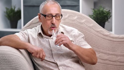 Adult Man Taking a Pill with Water Indoors