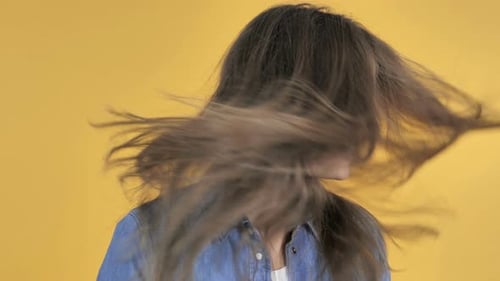 Smiling Brunette Woman Tossing Hair Against Yellow Backdrop