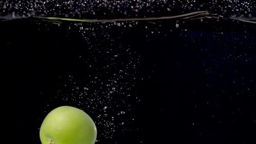 Vibrant green apple being dropped into water in slow motion.