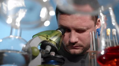 Man Looks into Microscope Surrounded by Lab Equipment
