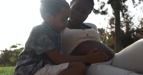 Mère enceinte africaine et fils ayant un moment tendre au parc de la ville en touchant le ventre
