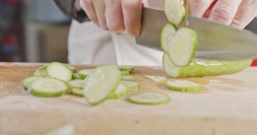 Slow motion close up of a chef knife slicing a cucumber