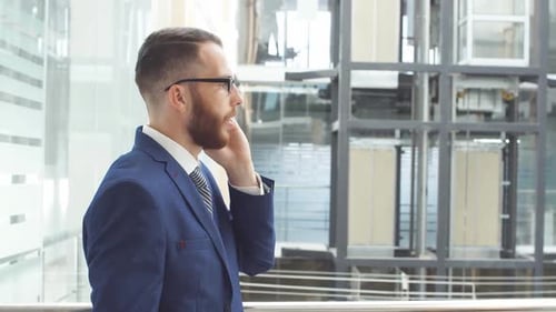 Young Businessman in Business Suit Uses Smartphone Standing in Lobby of Modern Business Center