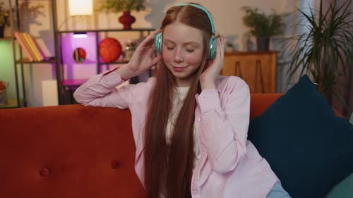 Happy Relaxed Kid in Wireless Headphones Dancing Listening Favorite Rock n Roll Music on Home Couch