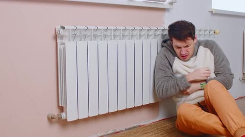 Man Sitting on Floor and Warming Near Radiator