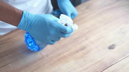 Person Cleaning Wooden Table with Spray Bottle