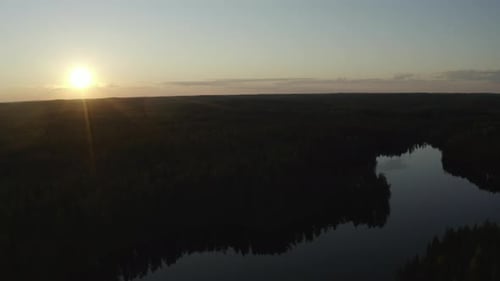 Drone view of sunset forest and lake. Flying to the left.