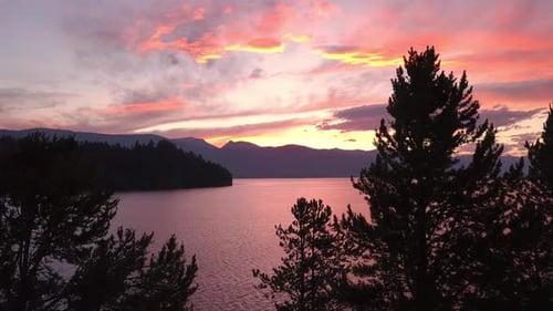 Rising slowly over trees viewing colorful sunset over lake