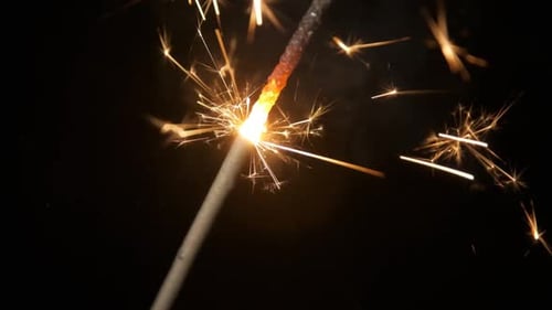 Sparkler Burning with Golden Sparks Against Black Backdrop