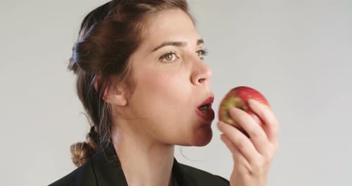 Woman eating a big red apple on a white studio background