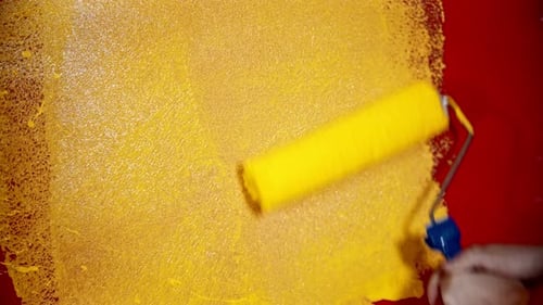 Eine Person malt eine leuchtend rote Wand mit gelber Farbe neu
