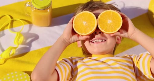 Child Lying on Blanket Hiding Behind Oranges