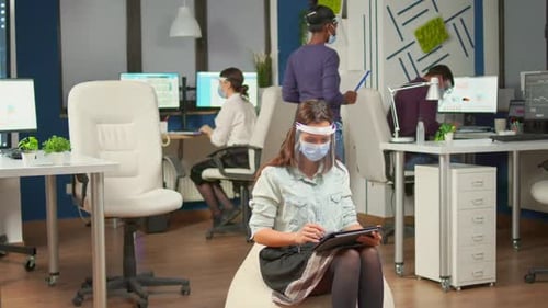 Businesswoman Sitting in Middle of Office Room Holding Digital Tablet