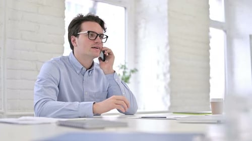 Attractive Working Young Man Talking on Smartphone in Office