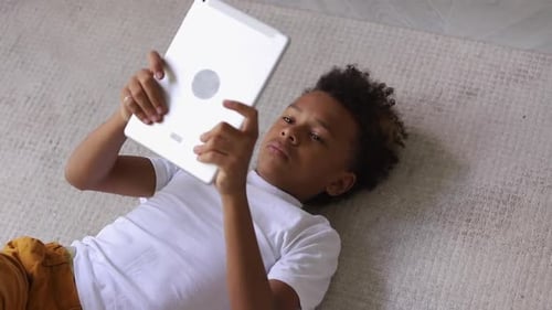 Boy Lies on Rug Using Tablet Device