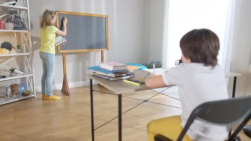 Breite Aufnahme eines positiven selbstbewussten Schulmädchens, das auf der Schulbehörde schreibt, als verschwommener Schuljunge sitzt