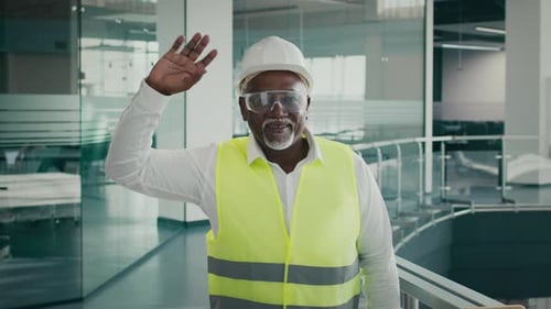 Black Civil Engineer In Protective Helmet Vest And Eyeglasses Waving At Camera