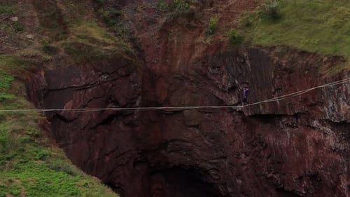 Aerial View on a Man Slacklining Over a Huge Dark Pit Extreme Sports