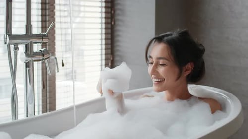 Glückliche Dame badet Spaß beim Blasen auf Schaum im Badezimmer
