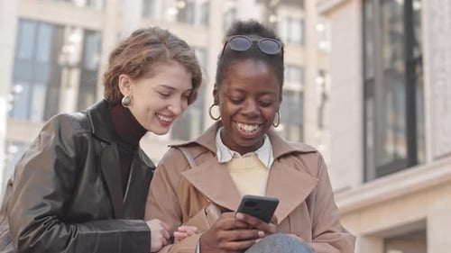 Two Smiling Women Using Phone Together in City