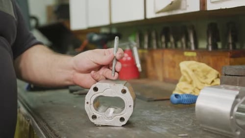 Kaukasischer Mann händet Fabrikarbeiter in einer Fabrik, der an einer Werkbank sitzt und an einem Metall arbeitet