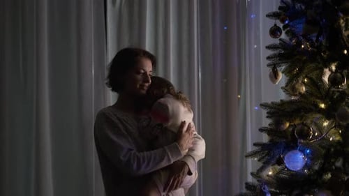 Woman Holding Child Looking at Christmas Tree